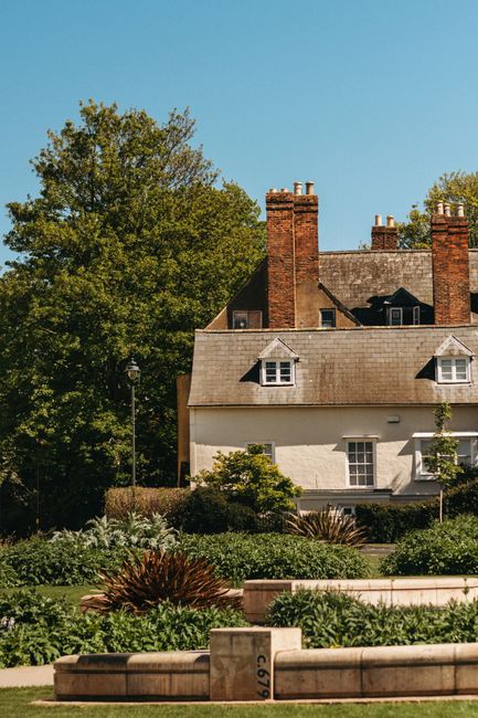 A well-maintained garden in the foreground features a variety of lush, green plants and bushes arranged in neatly bordered flower beds, with some plants exhibiting different textures, including spiky,