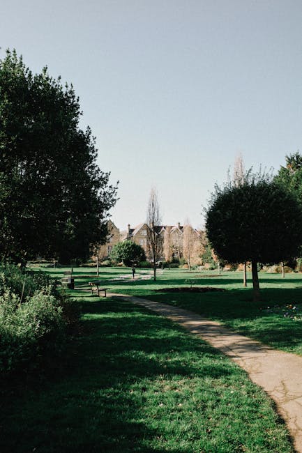 A well-maintained garden in the foreground features a variety of lush, green plants and bushes arranged in neatly bordered flower beds, with some plants exhibiting different textures, including spiky,