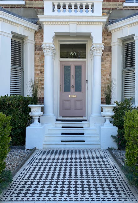 The photograph features the front entrance of a stately traditional house, showcasing a symmetrical facade with a pale mauve front door framed by classical white columns and decorative moulding. The d